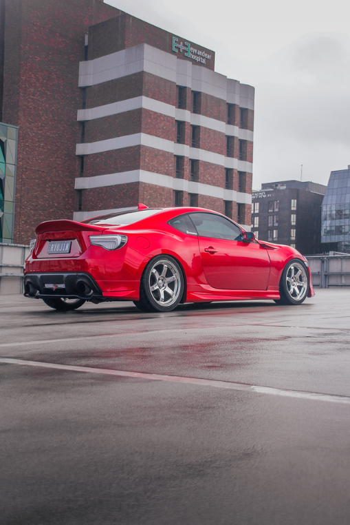 Red Toyota 86 on a wet rooftop car park with a brick hospital building behind
