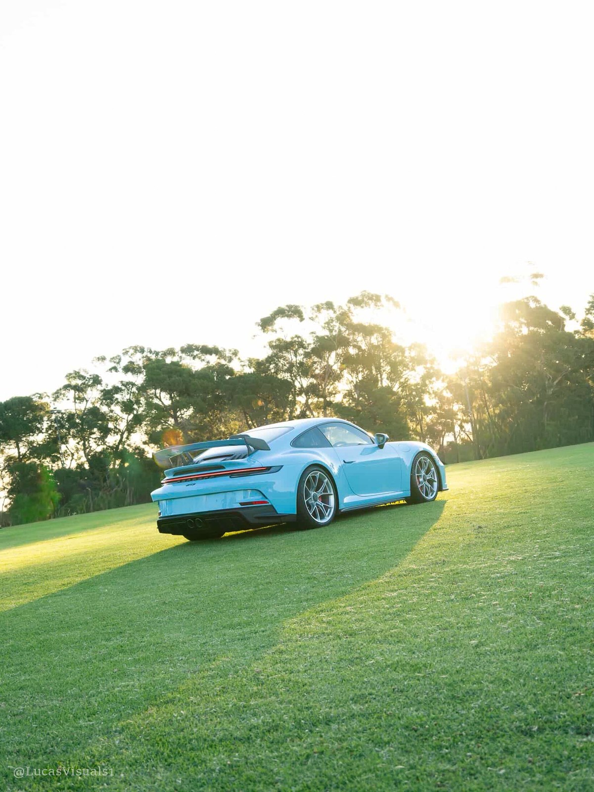 Baby blue Porsche 911 on grass at sunset
